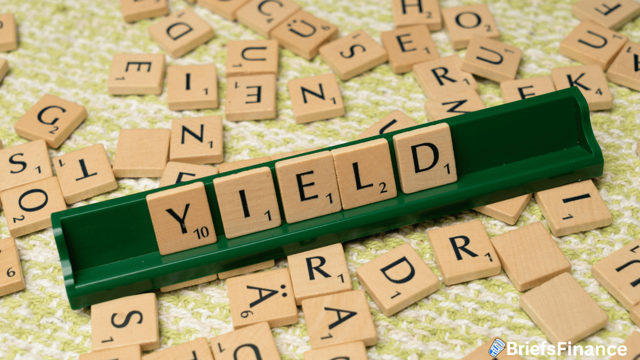 Scrabble tiles spell out the word "YIELD" on a green tile holder, with additional letter tiles scattered on a textured surface.