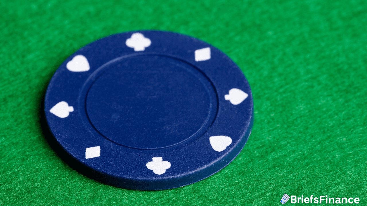 A blue poker chip with white suit symbols rests on a green felt surface, with the BriefsFinance logo in the bottom right corner.