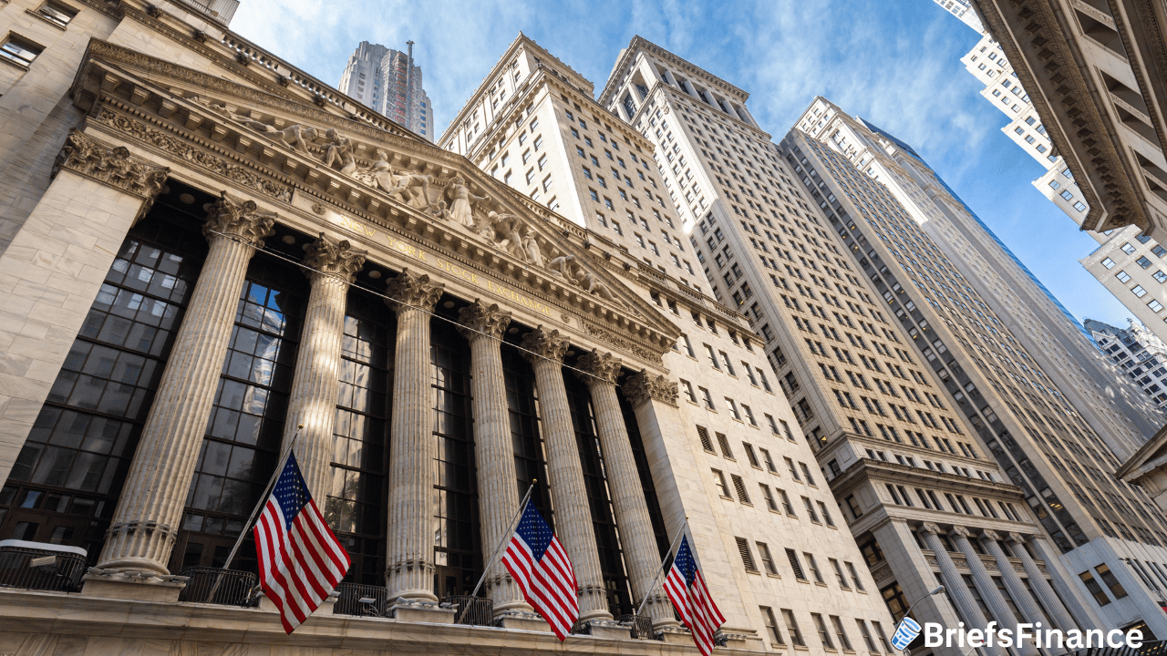 The New York Stock Exchange building with columns and American flags, surrounded by tall office buildings under a blue sky.