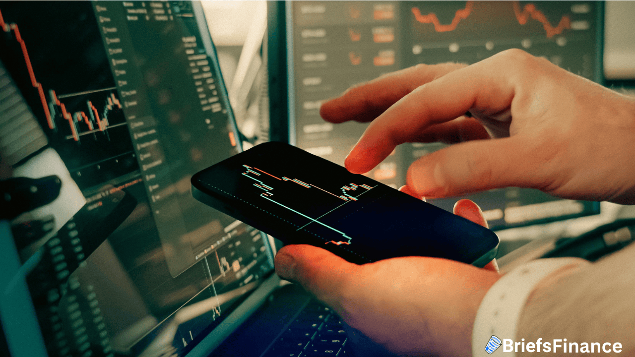 Person analyzing financial charts on a smartphone and computer, with multiple screens displaying stock market graphs.