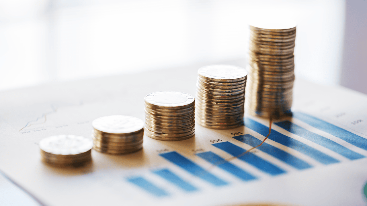 Stacks of coins are arranged in ascending order on a paper with bar graphs, representing financial growth or increasing profits.