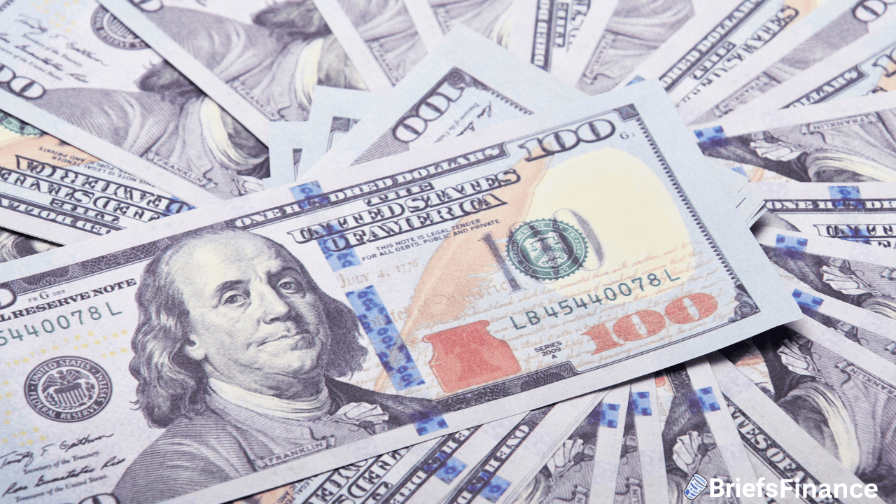 A spread of one hundred dollar bills fanned out, showing the portrait of Benjamin Franklin and security features.