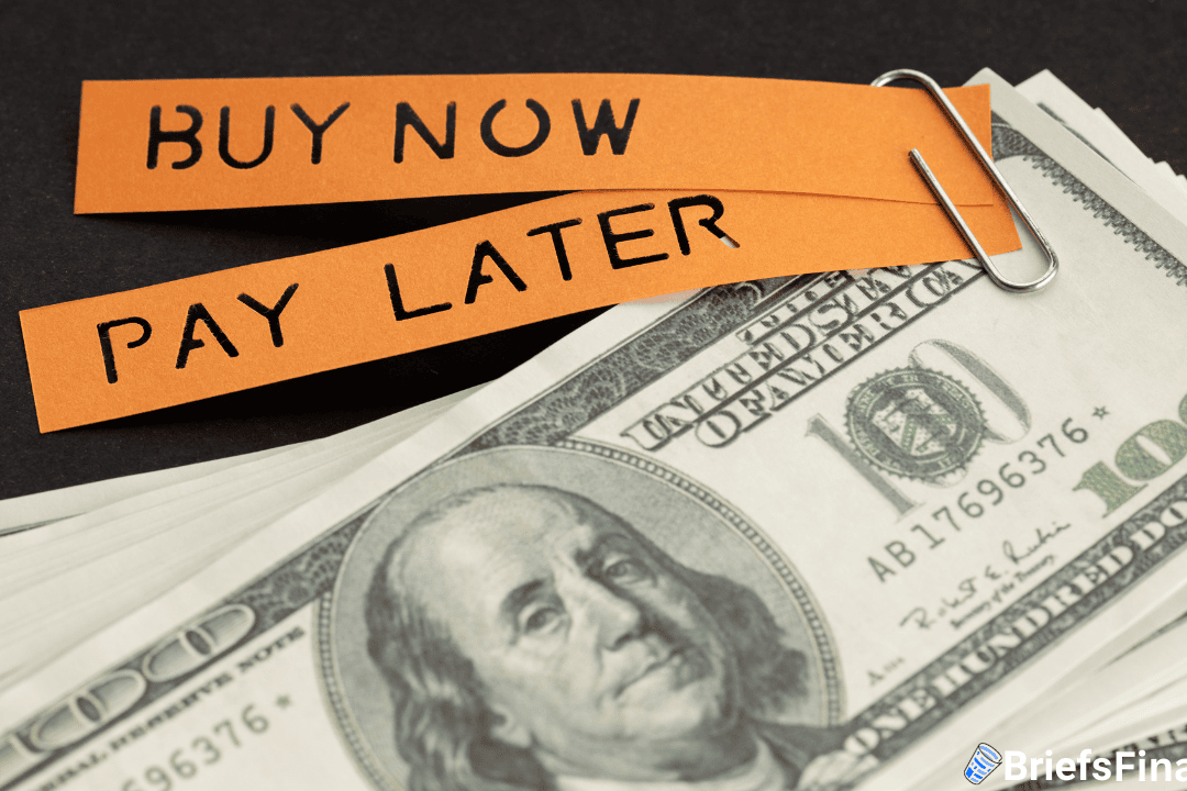 Orange paper strips reading "BUY NOW PAY LATER" are clipped together and placed above a stack of $100 bills.