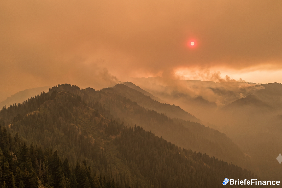 Wildfire smoke over a forested mountain ridge with a red sun