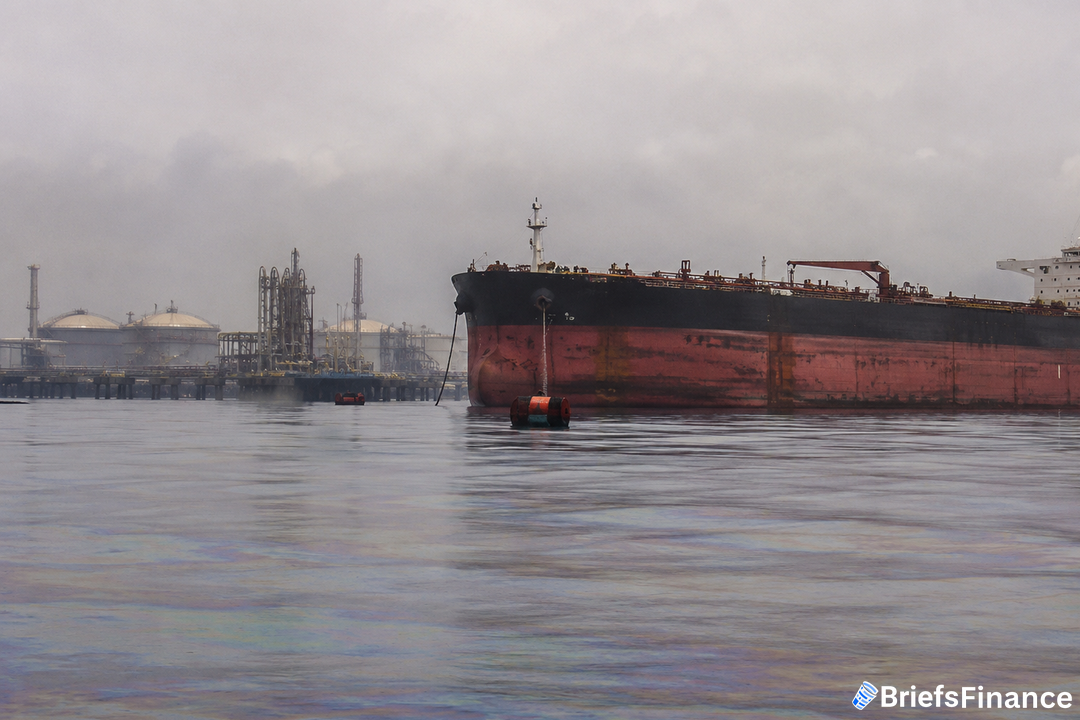 Crude oil tanker idling at anchor near a hazy industrial export terminal